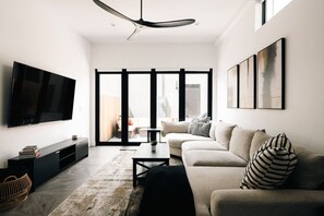 A modern living room with a flat-screen TV, a sofa, a coffee table, and a large window with a view to the outside. - Luxury RINO Townhome, Walk to Everything! (Denver)