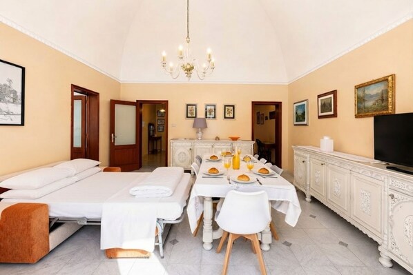 Una camera da letto con un letto, un tavolo da pranzo apparecchiato con piatti e bicchieri, una televisione e un lampadario.