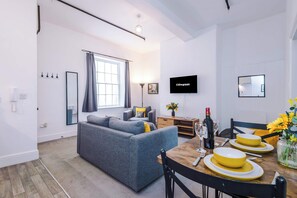 Ein modernes Wohnzimmer mit einem grauen Sofa, einem Esstisch mit gelben Tellern und einem an der Wand montierten Flachbildfernseher.