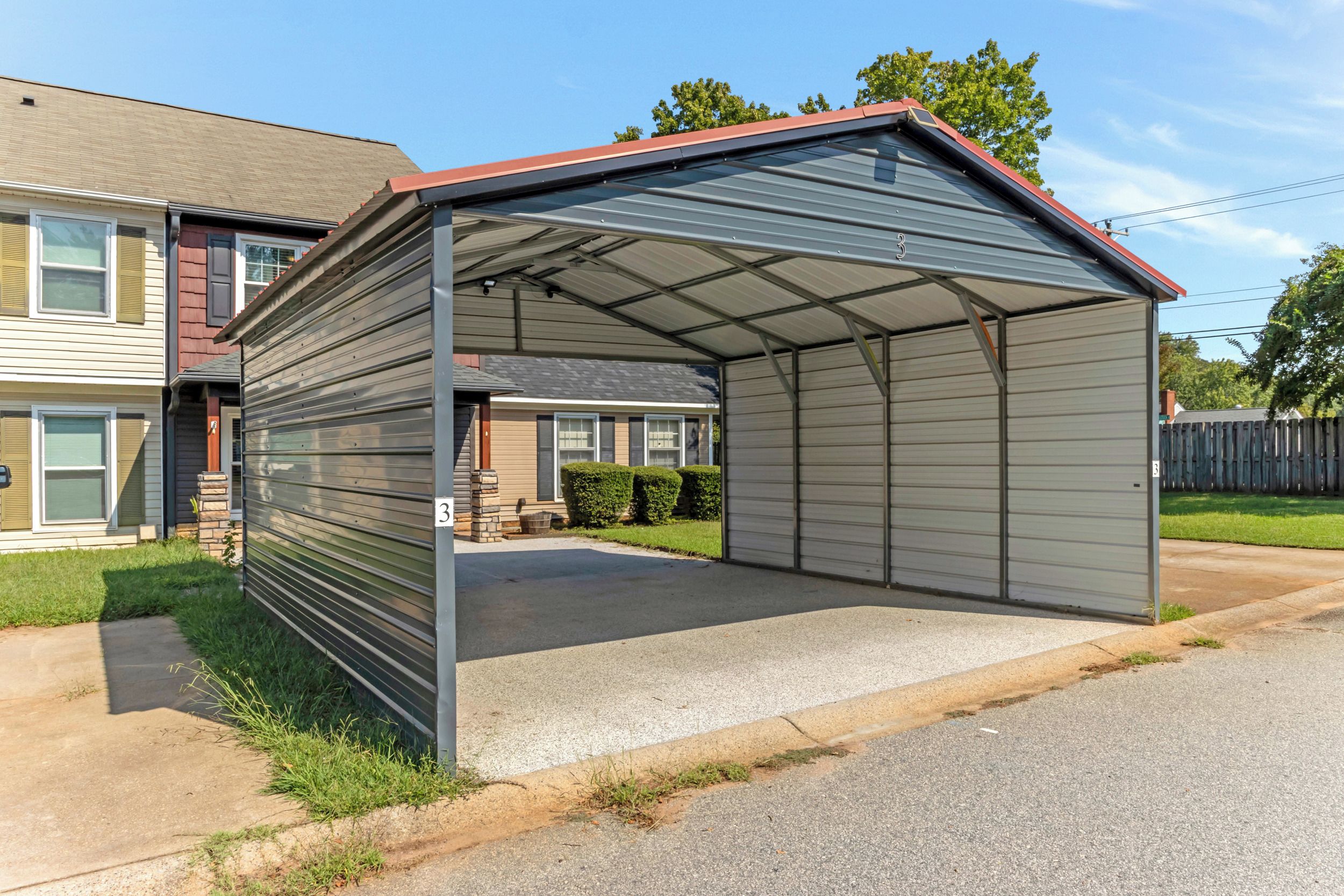 Ein Metall-Carport mit Satteldach, neben einem Wohngebäude.