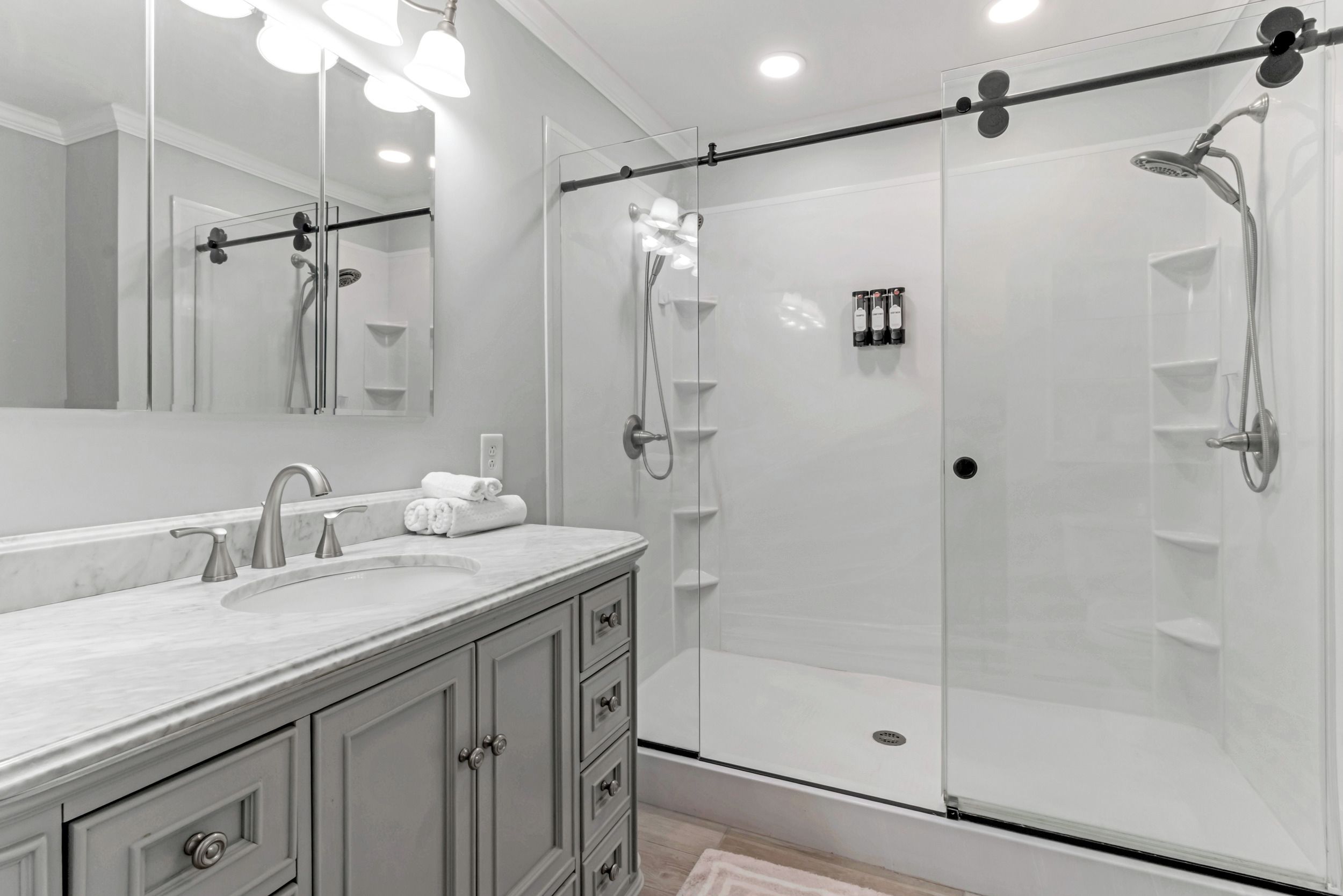 A modern bathroom with a large mirror, a sink, and a walk-in shower.
