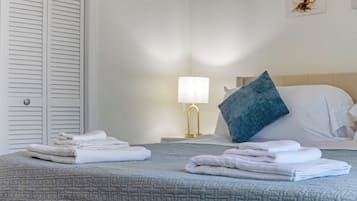 Ein ordentlich gemachtes Bett mit gefalteten Handtüchern, einer Nachttischlampe und einem Wandbild.