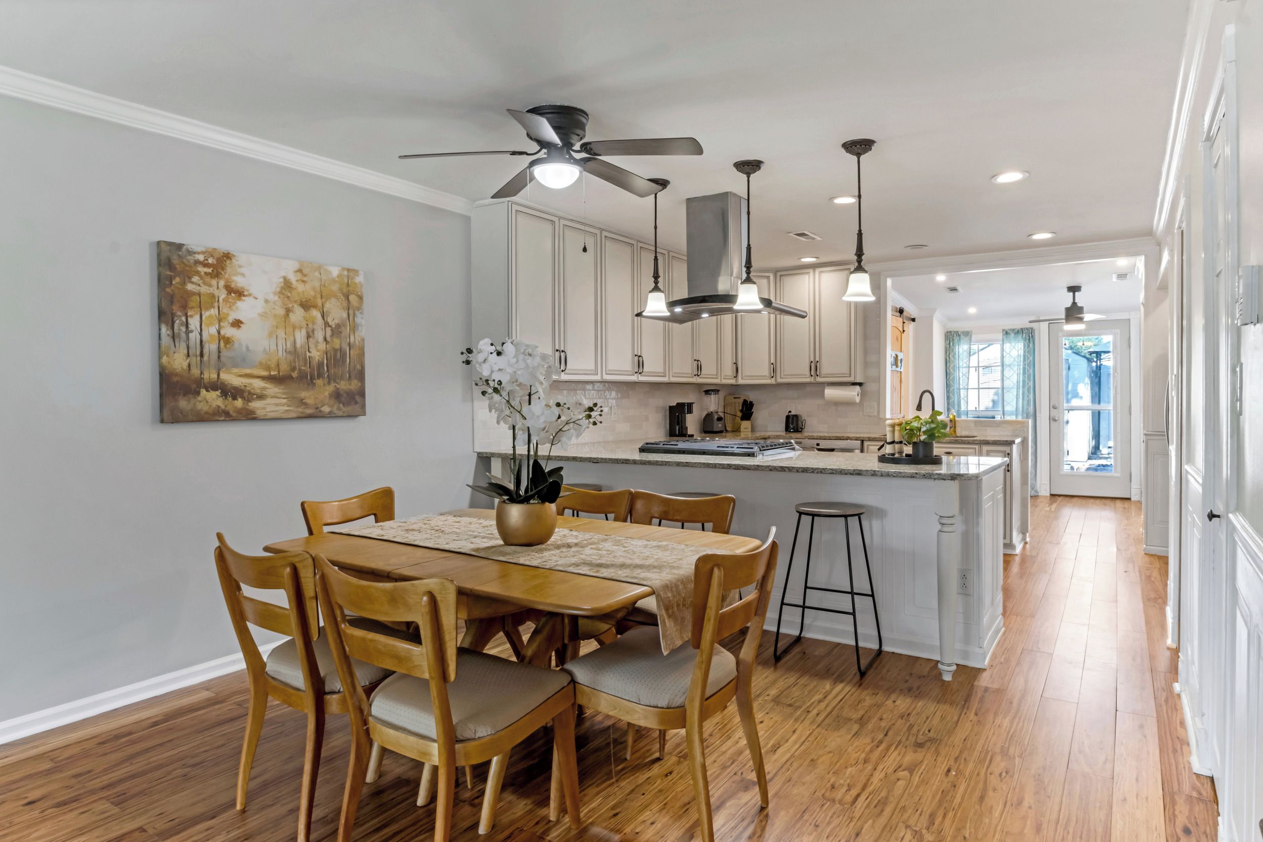 A modern kitchen with white cabinets, a dining area with wooden chairs, and a ceiling fan.
