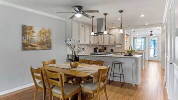 A modern kitchen with white cabinets, a dining area with wooden chairs, and a ceiling fan.