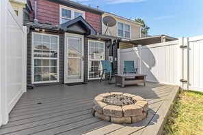 Eine Terrasse mit Feuerstelle, Sitzgelegenheiten im Freien und einem weißen Zaun.