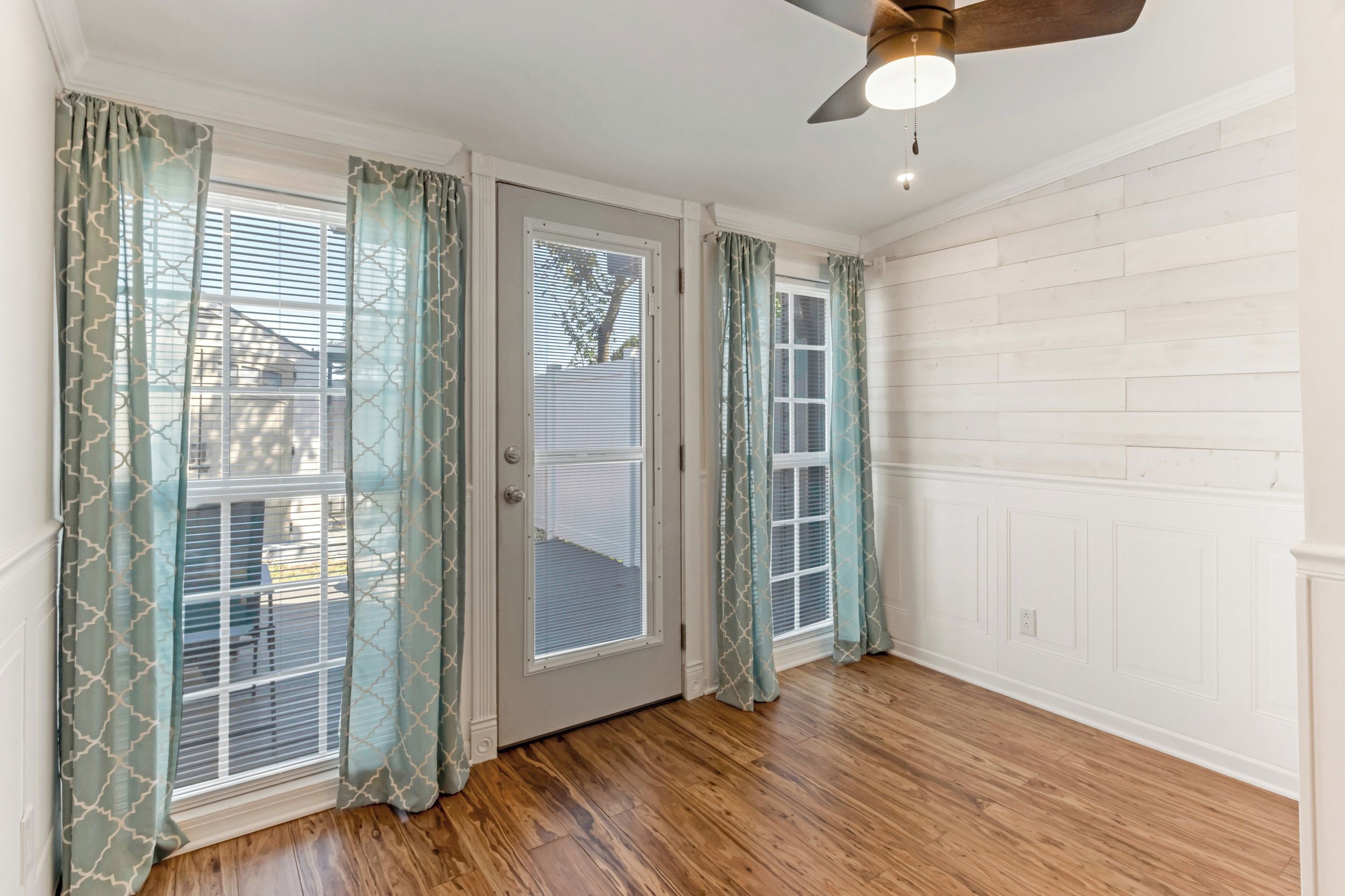 A room with a wooden floor, white walls, and a ceiling fan.