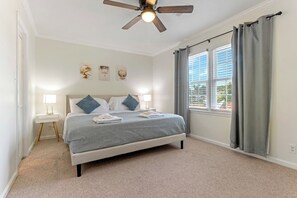 Quarto com cama, abajures, ventoinha no teto e janela com cortinas.