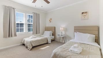 Ein Hotelzimmer mit zwei Betten, einem Deckenventilator, einem Fenster mit Jalousien, einer Nachttischlampe und Bildern an der Wand.