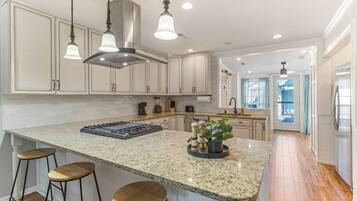A kitchen with a large island, bar stools, a stove, and pendant lighting.