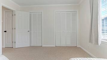 A bedroom with a carpeted floor, a bed, two white closets, and a window with blinds.