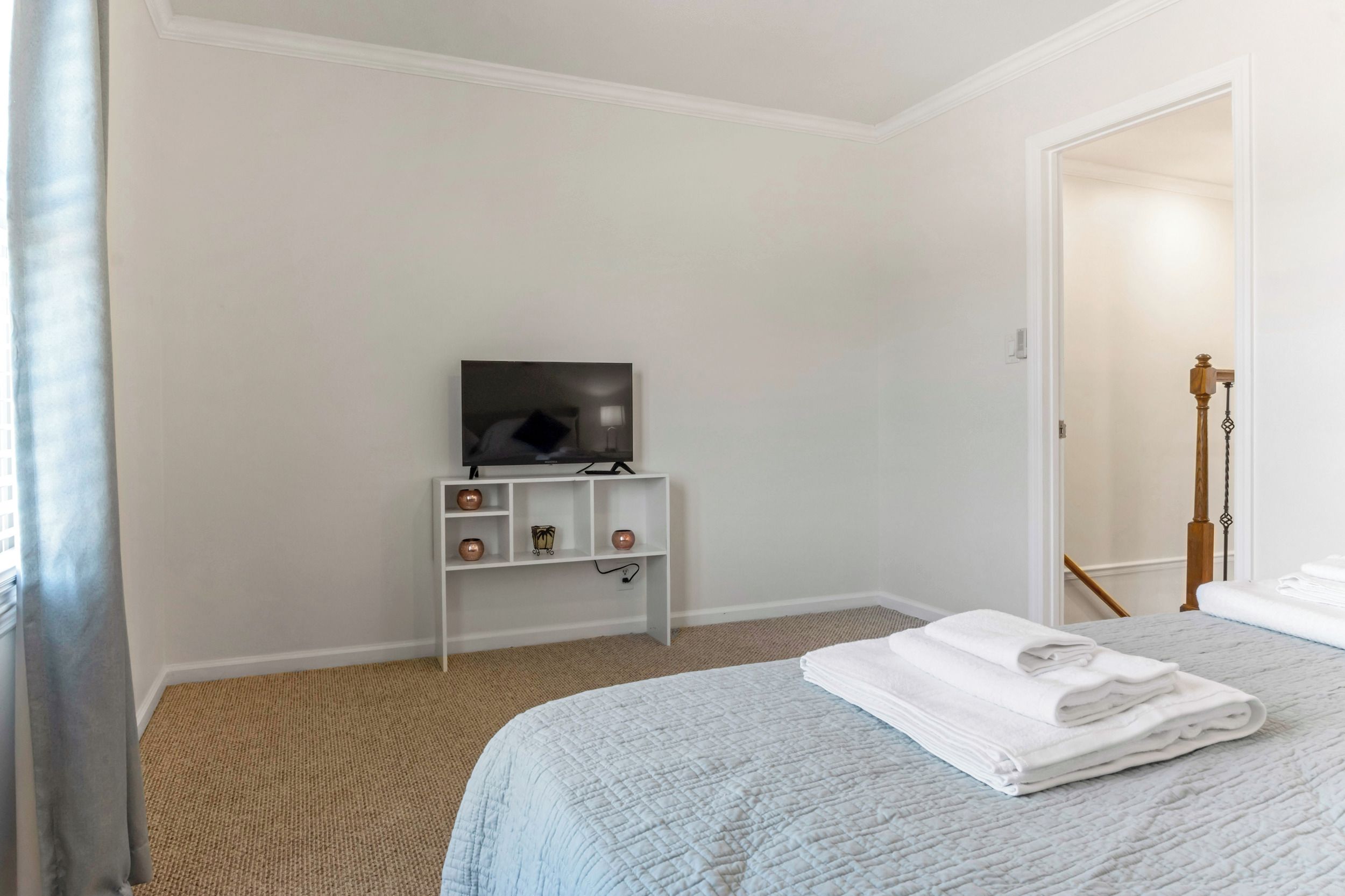 Habitación de hotel con cama, televisor sobre un soporte, estante con adornos y puerta que da a otra habitación.
