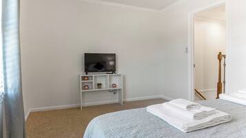Habitación de hotel con cama, televisor sobre un soporte, estante con adornos y puerta que da a otra habitación.