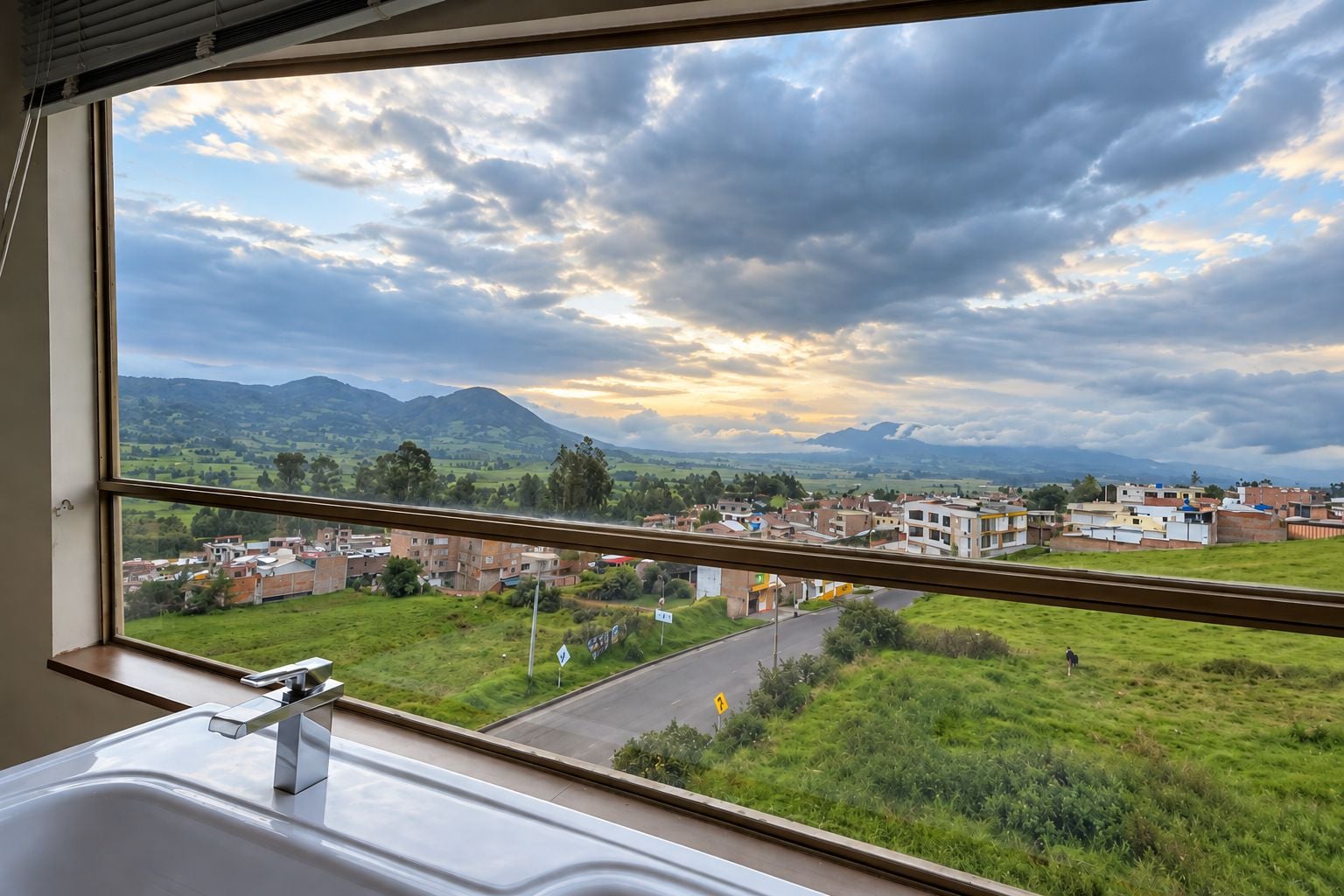 A bathroom with a window overlooking a rural landscape with buildings and mountains.