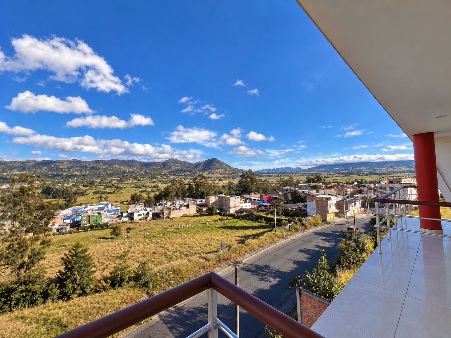Un balcón con vistas a un pueblo, montañas y un cielo despejado.