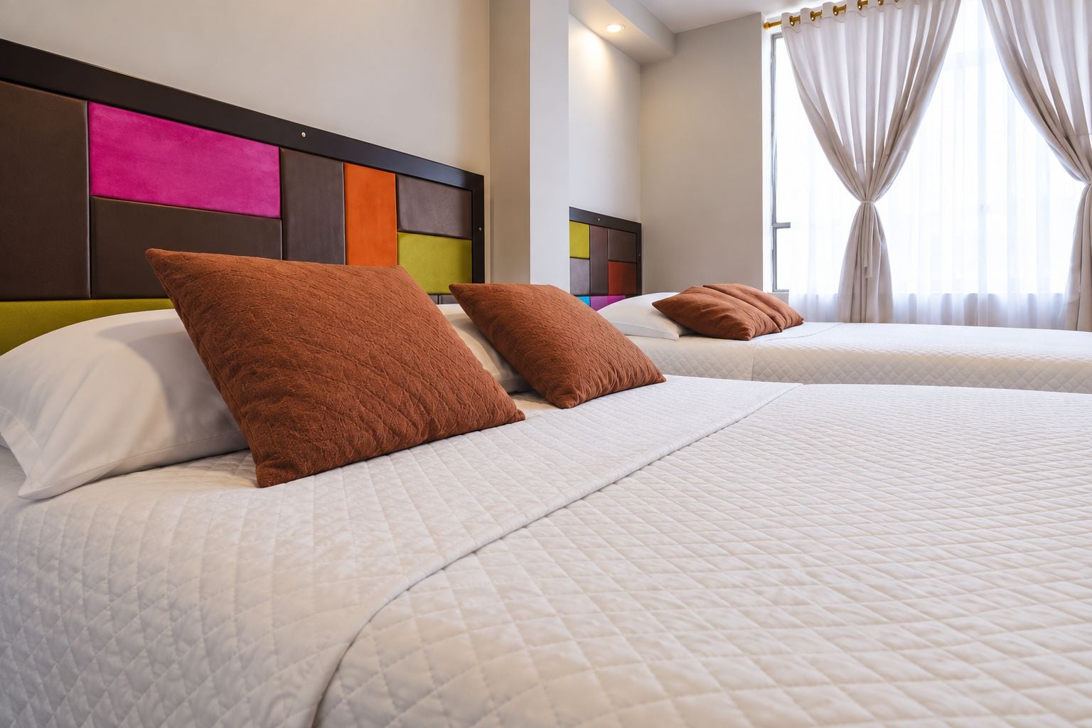 Une chambre d’hôtel avec deux lits, chacun étant équipé de draps blancs et d’oreillers marron.
