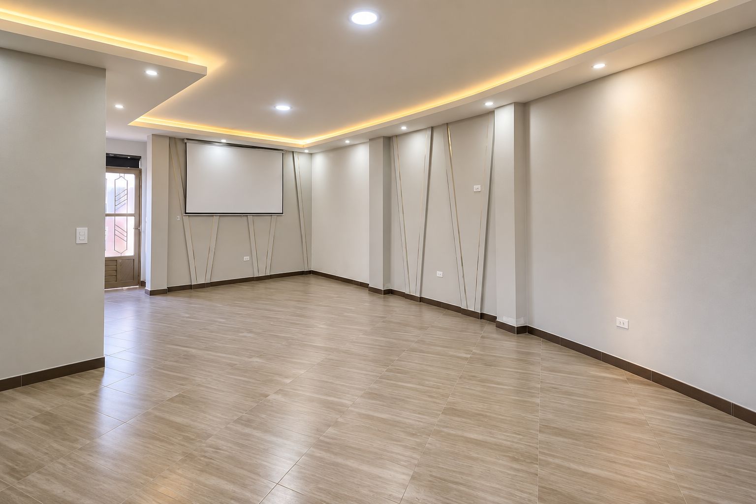 A spacious room with a wooden floor, recessed ceiling lighting, and a large wall-mounted screen.