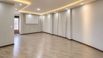A spacious room with a wooden floor, recessed ceiling lighting, and a large wall-mounted screen.