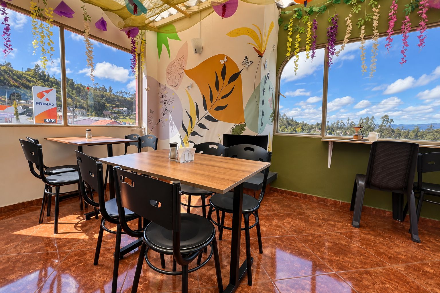 Ein Restaurant mit Holztisch, schwarzen Stühlen, einer Wandmalerei und Blick auf die Hügel.