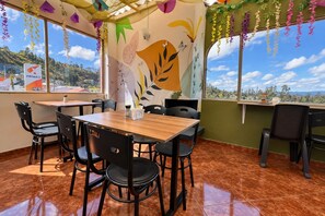 A restaurant with a wooden table and black chairs, a mural on the wall, and a view of the hills. - HOTEL NALNOA REAL (Guachucal)