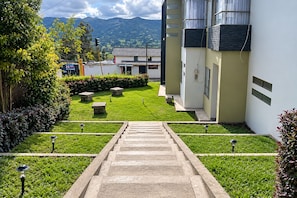 Un sendero conduce a un edificio de diseño moderno, rodeado por un jardín bien cuidado con césped y arbustos.