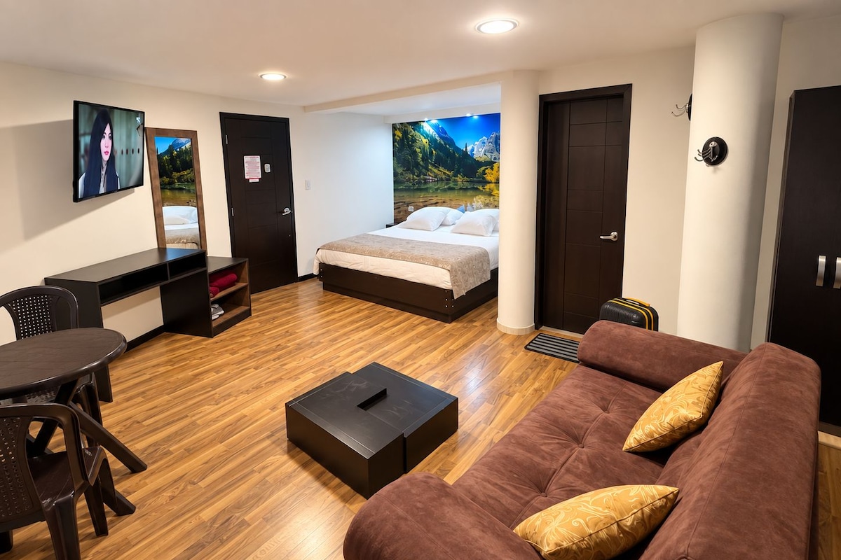 A modern hotel room with a bed, a sofa, a desk, and a TV.