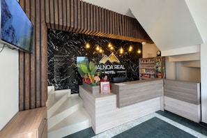 Una recepción de hotel con diseño moderno, una pared de mármol y un letrero que dice 'ALINOA REAL HOTEL'.