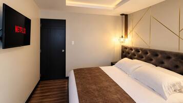 Habitación de hotel con una cama, televisor montado en la pared, una puerta y una lámpara también fijada a la pared.