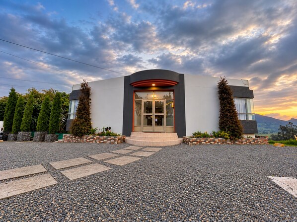 A modern building with a curved entrance, a glass door, and a gravel driveway.