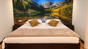 Un dormitorio con una cama, dos almohadas y un amplio mural en la pared que muestra un paisaje montañoso.