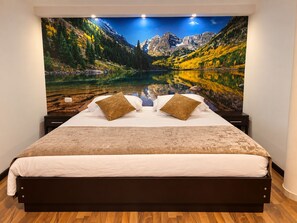 Un dormitorio con una cama, dos almohadas y un amplio mural en la pared que muestra un paisaje montañoso.