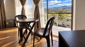 Una habitación con piso de madera, una mesa redonda, dos sillas y vista a un paisaje a través de amplios ventanales.