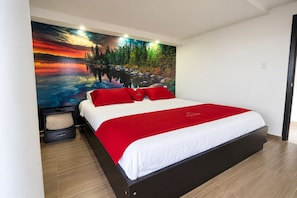 A bedroom with a bed, a red blanket, and a wall mural of a landscape.