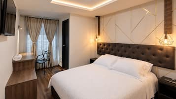 Una habitación de hotel moderna con una cama grande, un escritorio con una silla, un televisor de pantalla plana montado en la pared y una lámpara en el techo.