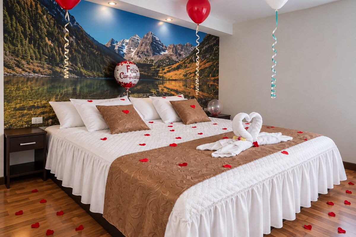 A hotel room with a bed, pillows, a swan-shaped towel arrangement, and a scenic mountain view.