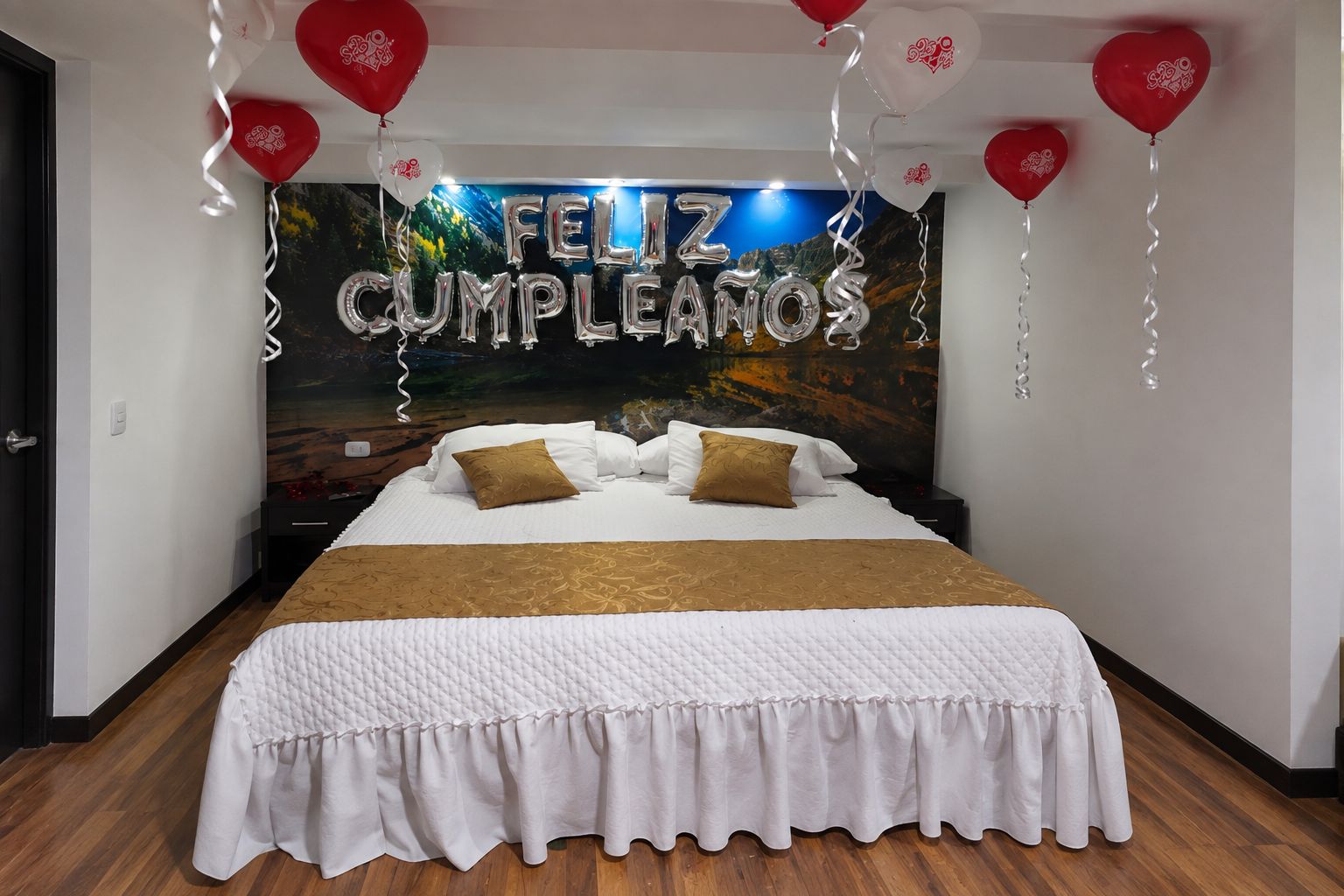 A bedroom with a bed, pillows, a wall mural, and balloons.