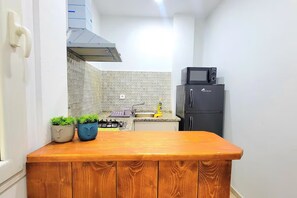 A narrow kitchen with a wooden countertop, a black refrigerator, and a microwave. - Au cœur de la MARSA (Marsa)