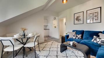 A modern living room with a blue sofa, a coffee table, and a dining area with a glass table and chairs.
