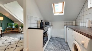A compact kitchen with a microwave, oven, and washing machine. A skylight provides natural light. - Stephenson View (Newcastle upon Tyne)