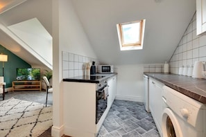Eine kompakte Küche mit Mikrowelle, Backofen und Waschmaschine. Ein Dachfenster sorgt für natürliches Licht.