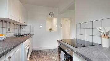 A modern kitchen with white cabinets, a built-in oven, a washing machine, and a tiled backsplash.