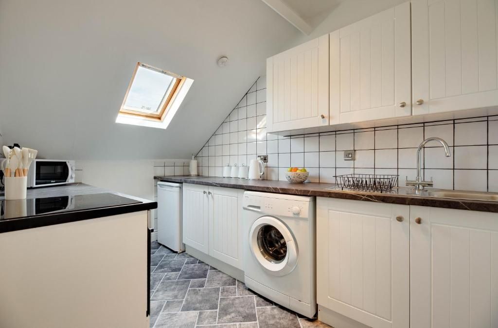 A modern kitchen with a skylight, white cabinets, a built-in washing machine, and a tiled backsplash.