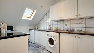 A modern kitchen with a skylight, white cabinets, a built-in washing machine, and a tiled backsplash.