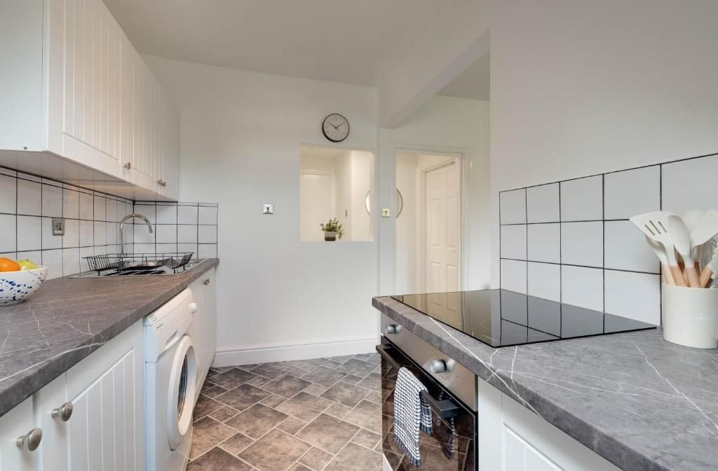 Ett modernt kök med vita skåp, en inbyggd ugn, en tvättmaskin och en kakelbeklädd vägg bakom arbetsbänken.