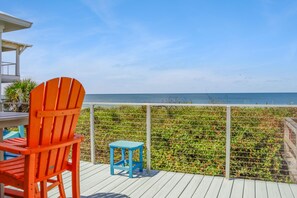 A wooden deck with a red chair and a blue table, overlooking a beach with a metal fence. - Summer Salt (Port St. Joe)