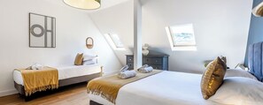 Ein Hotelzimmer mit zwei Betten, einem Fenster mit Blick, einem Wandbild und einem kleinen Tisch mit einer Lampe.