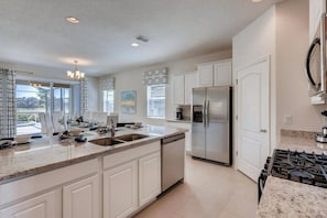A modern kitchen with white cabinetry, a stainless steel refrigerator, a gas stove, and a large window providing natural light. - Poolside Paradise!

Poolside Paradise! (Davenport)
