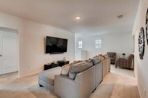 A living room with a grey sofa, a flat-screen TV, a small table with a lamp, and a patterned armchair. - Poolside Paradise!

Poolside Paradise! (Davenport)