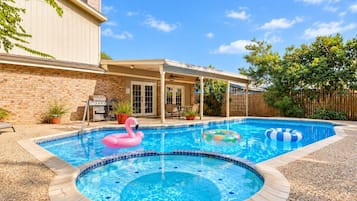 A backyard with a swimming pool, a barbecue grill, and a covered patio area.