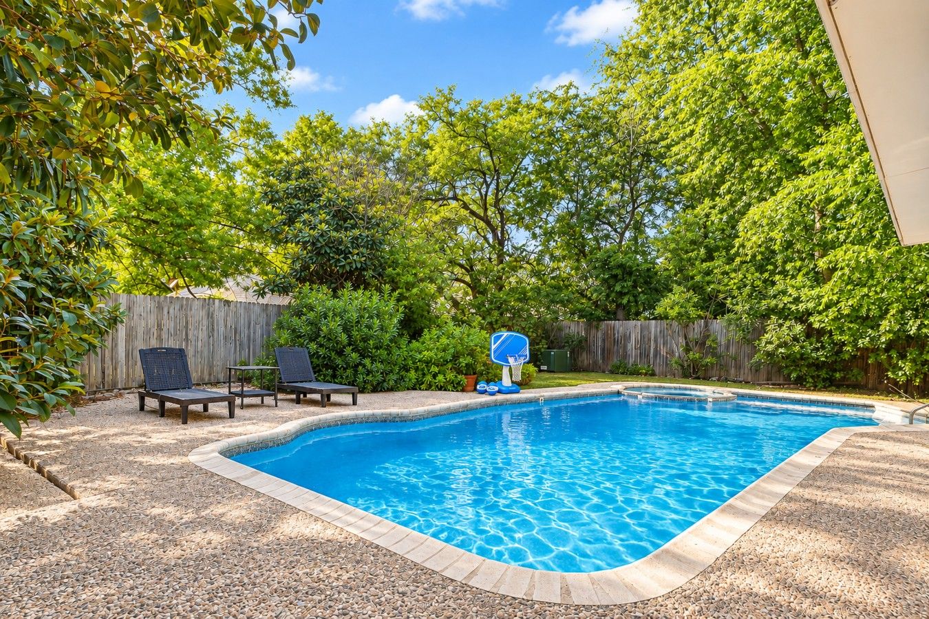 A backyard with a swimming pool, a basketball hoop, and two lounge chairs.
