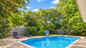 Un jardin avec une piscine, un panier de basketball et deux chaises longues.